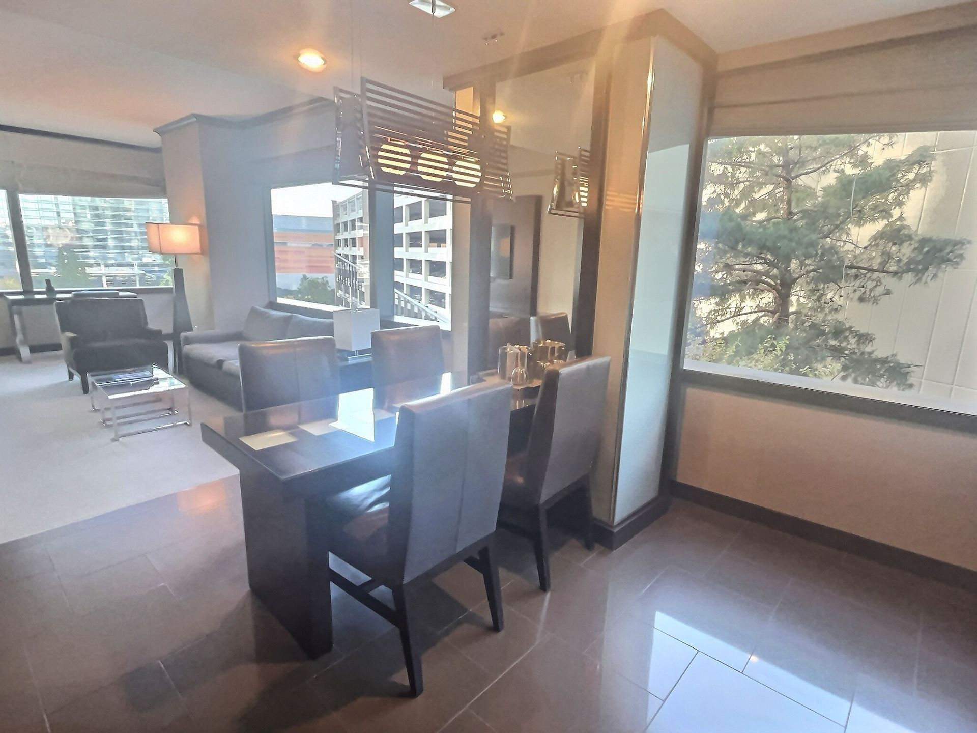Modern living and dining area with large windows, dark furniture, and city views