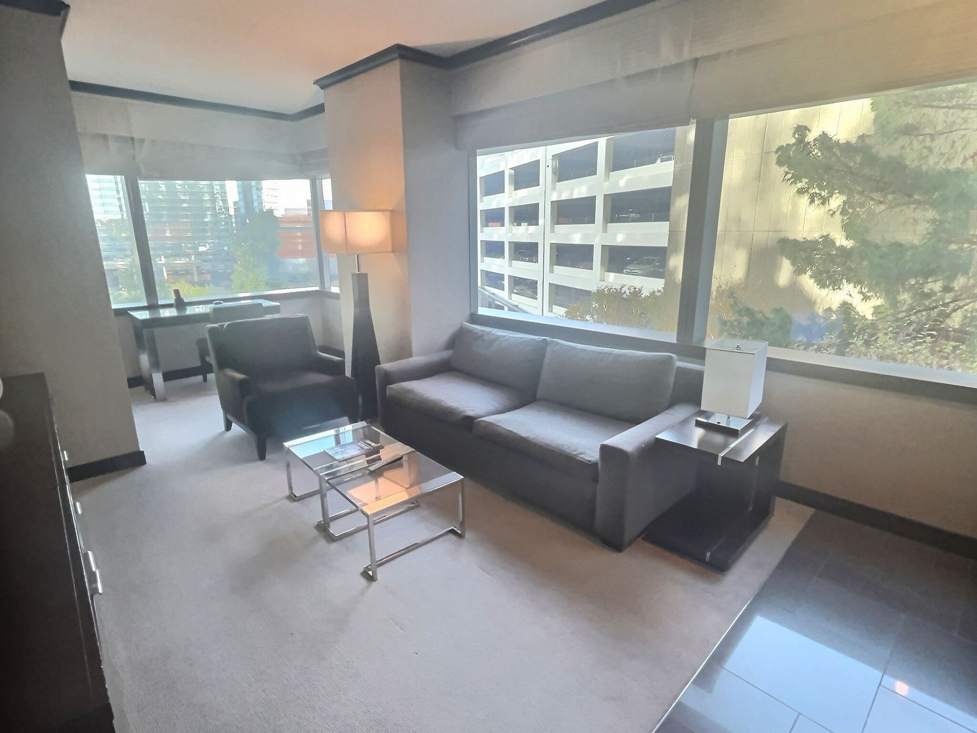 Modern office lounge with gray sofa, glass coffee table, armchair, and large windows