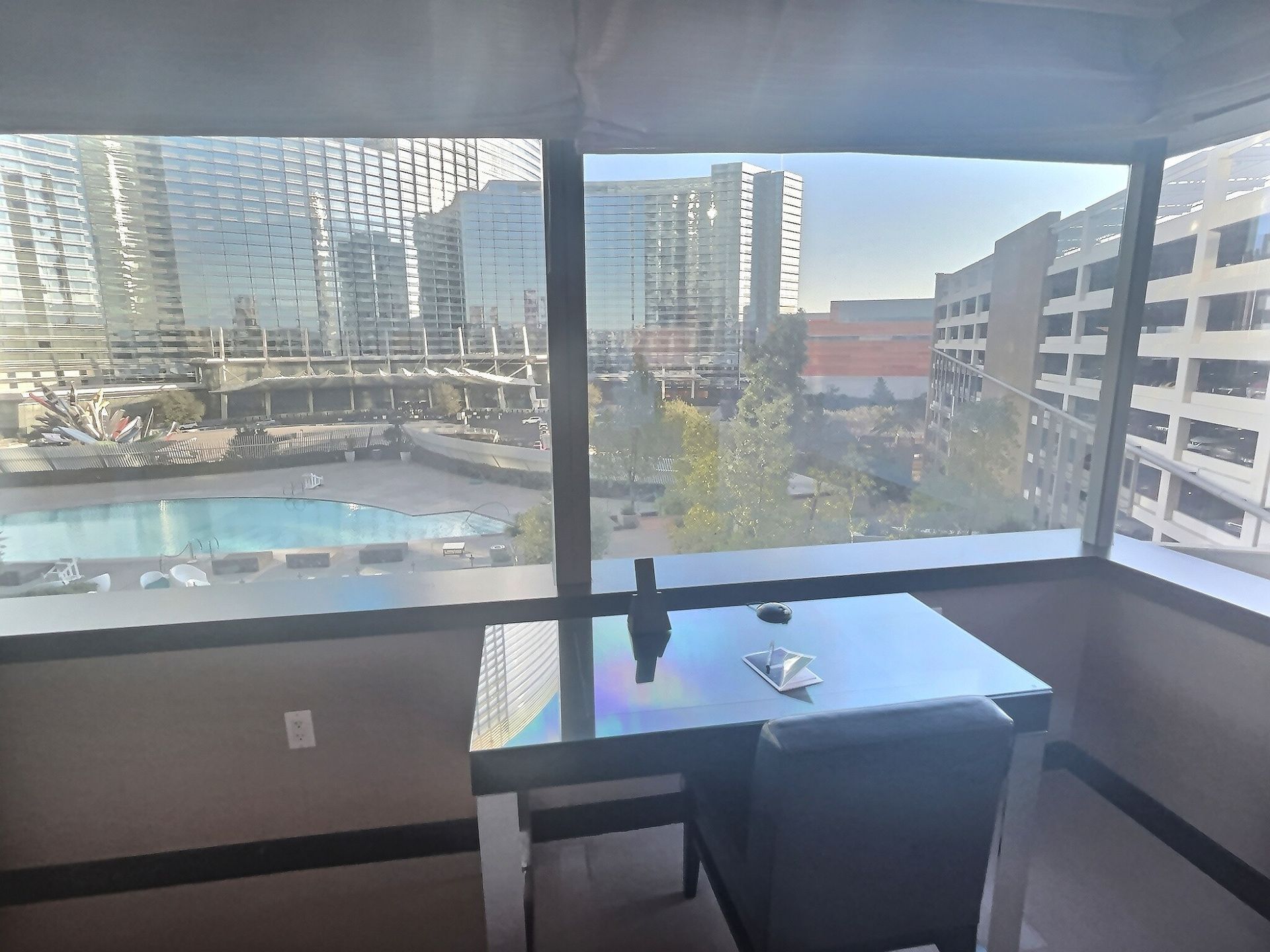 Balcony with glass railing, table and chair, overlooking a pool and city buildings at sunset