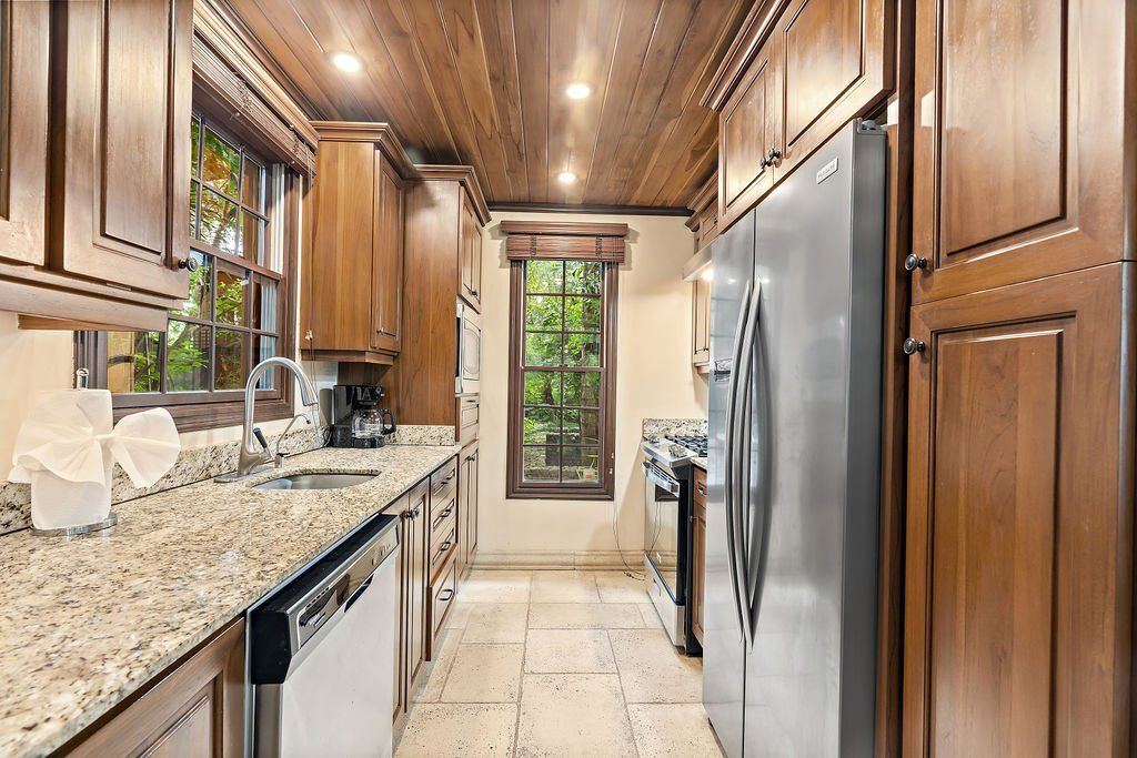 Narrow kitchen with wood cabinets, granite counters, stainless appliances, and a door at the end.