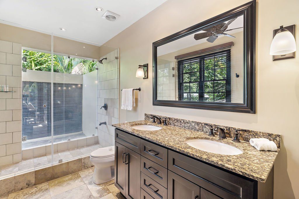Bright bathroom with granite vanity, large mirror, and glass-enclosed shower near a window.
