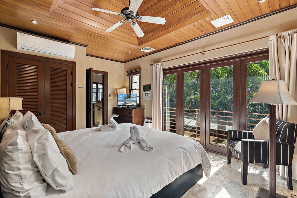 Spacious tropical bedroom with a large bed, wood ceiling, ceiling fan, and sliding glass doors to a patio