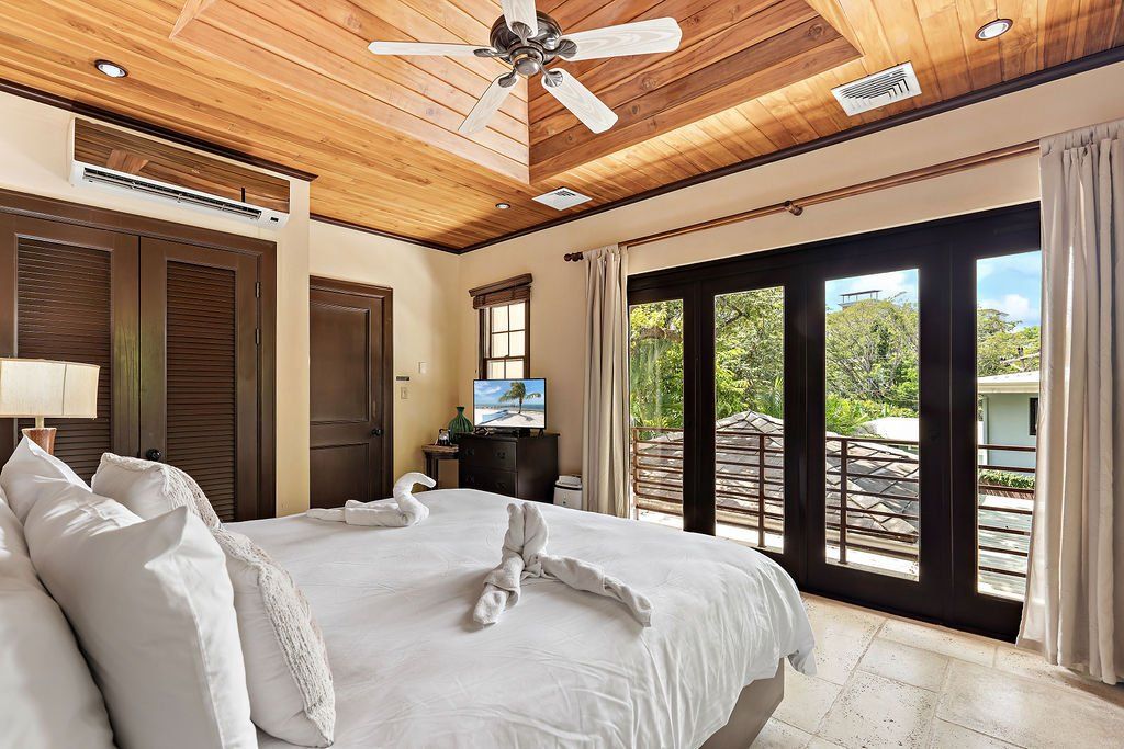 Bright bedroom with king bed, wood ceiling, ceiling fan, and sliding glass doors to a patio.