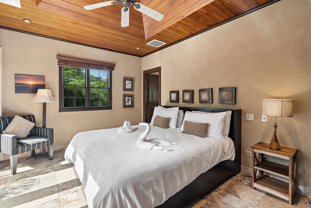 Bright bedroom with a large bed, wood ceiling, lamps, chairs, and framed art.