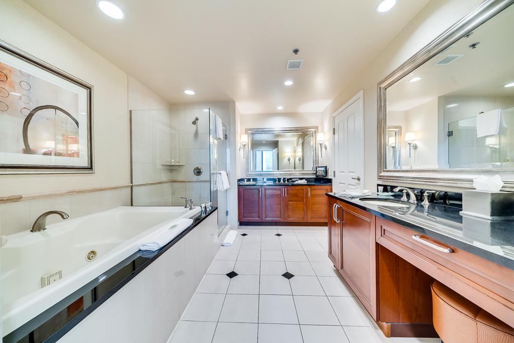 Bright bathroom with twin sinks, a soaking tub, glass shower, and white tile flooring
