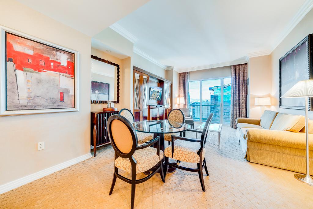 Bright living room with glass coffee table, beige sofa, wall art, and sliding doors to a balcony