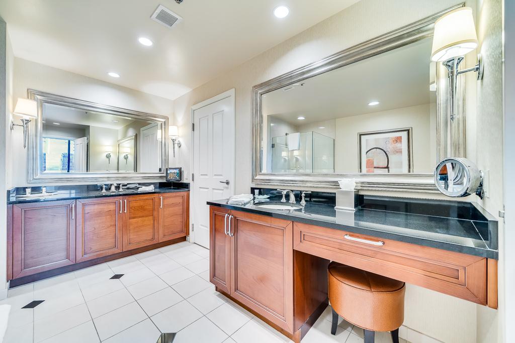 Bright bathroom with double vanity, large mirrors, white tile floor, and wood cabinets.