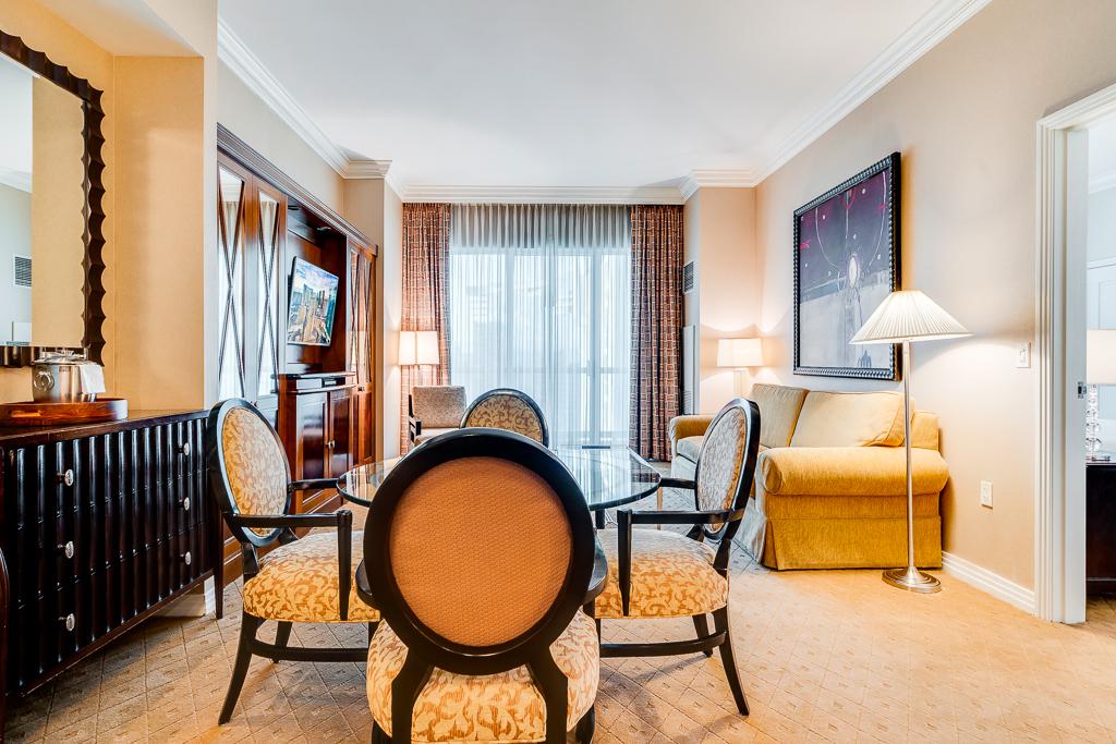 Elegant hotel room with round table, chairs, yellow sofa, and large window with curtains