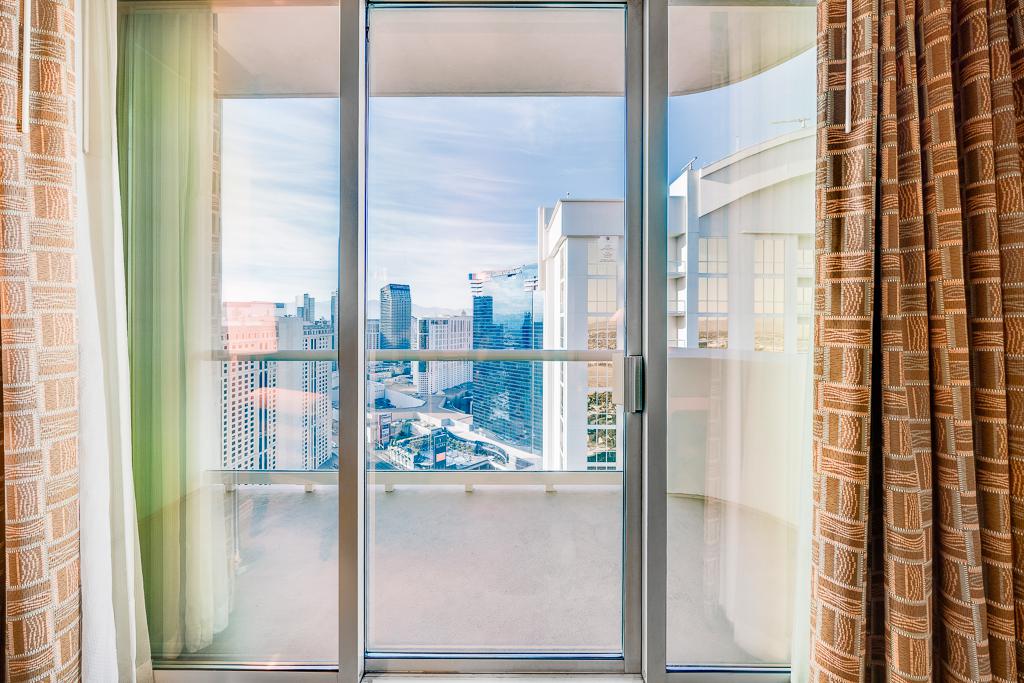 Sliding glass doors open to a bright city view, framed by curtains in a modern room.