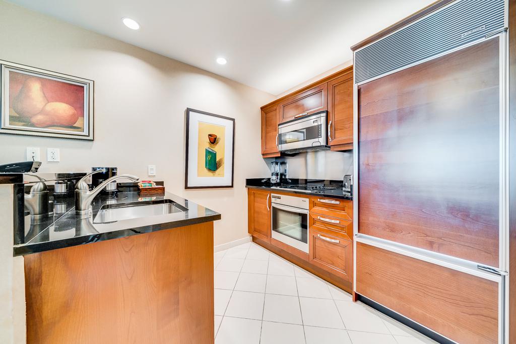 Modern kitchen with wood cabinets, black countertops, white tile floor, and stainless steel appliances