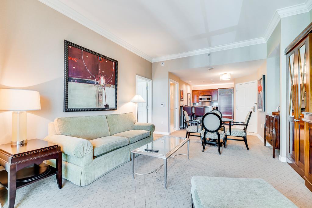 Bright living room with sofa, glass coffee table, dining area, and large windows