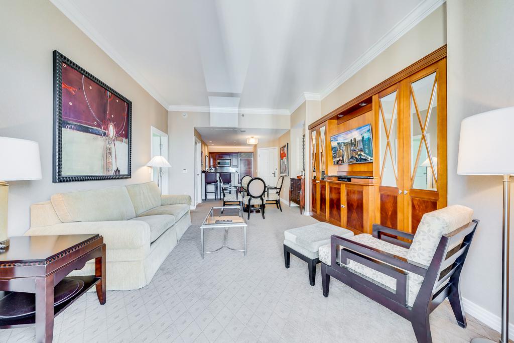 Bright living room with cream sofa, dark chairs, floor lamps, and wood cabinets along the wall.