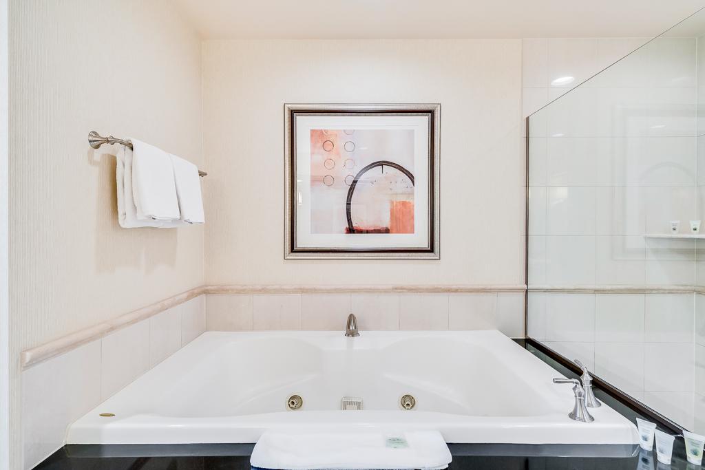 Bright bathroom with a white bathtub, towel rack, glass shower door, and framed artwork.