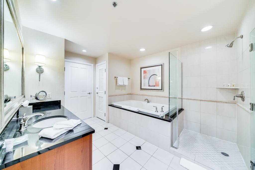 Bright white bathroom with double vanity, large mirror, bathtub, and tiled floor