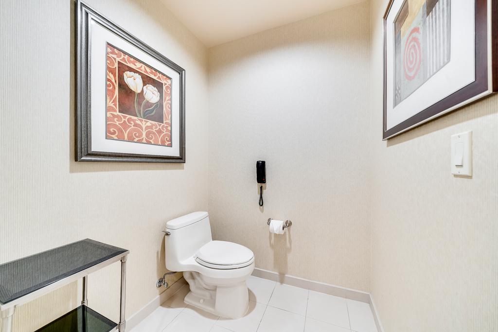 Small restroom with a toilet, framed wall art, and beige walls under bright lighting