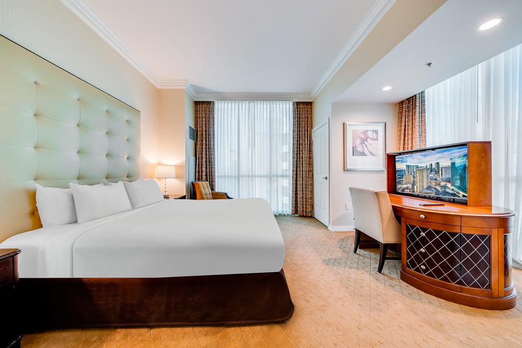 Modern hotel room with king bed, large TV, desk, and floor-to-ceiling windows