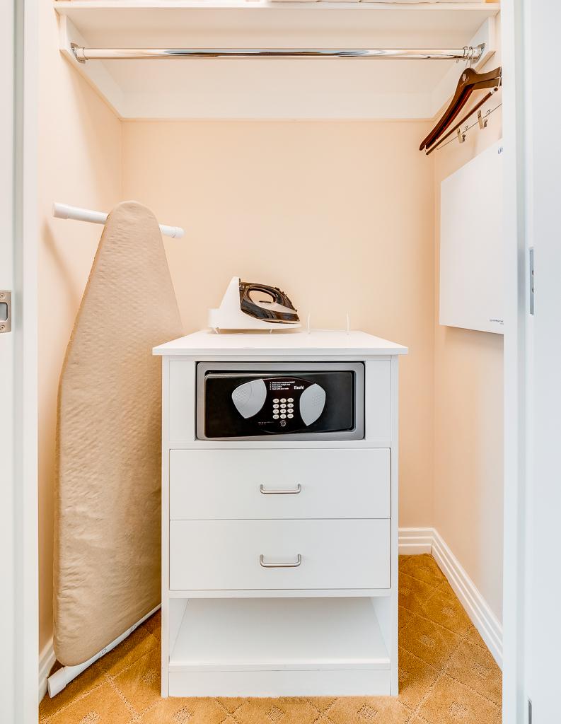Small beige closet with a white dresser, ironing board, and hanging clothes rod.