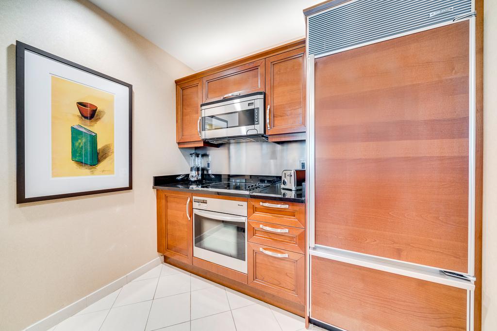 Compact kitchen with wood cabinets, stainless appliances, and framed wall art