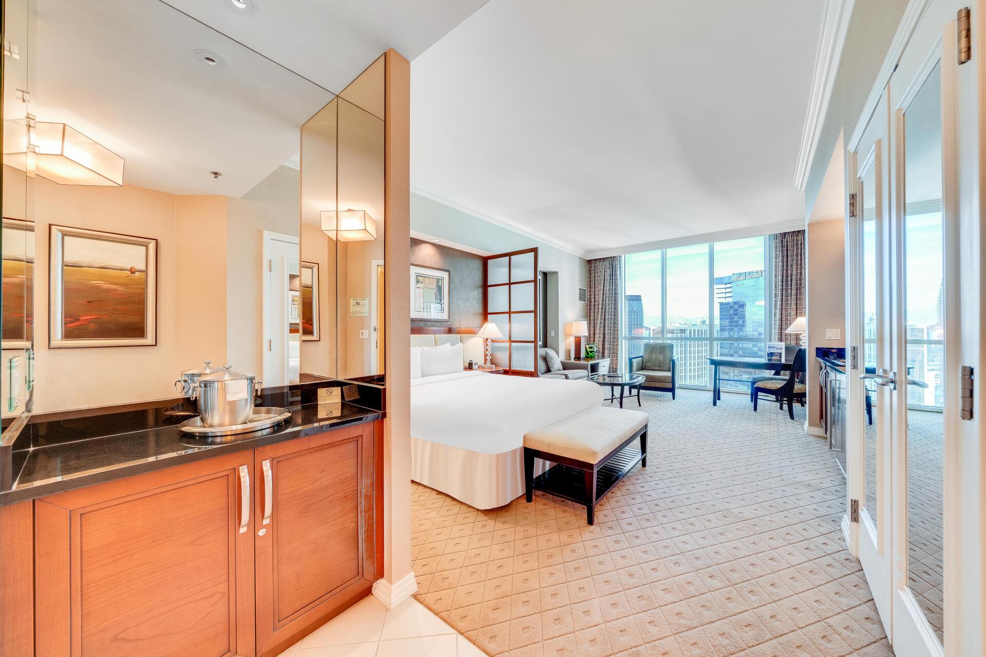 Luxury hotel room with king bed, work desk, and floor-to-ceiling windows overlooking the city.
