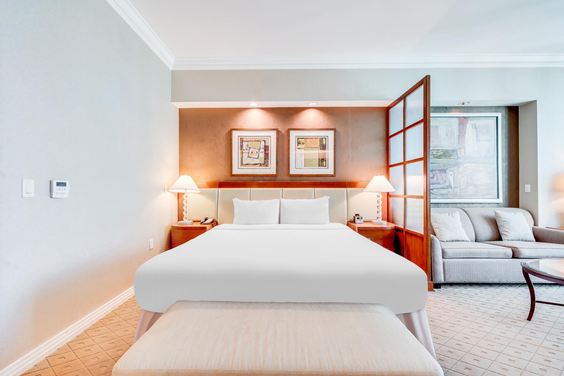 Modern bedroom with a white bed, orange wood partition, and adjacent sitting area by a window