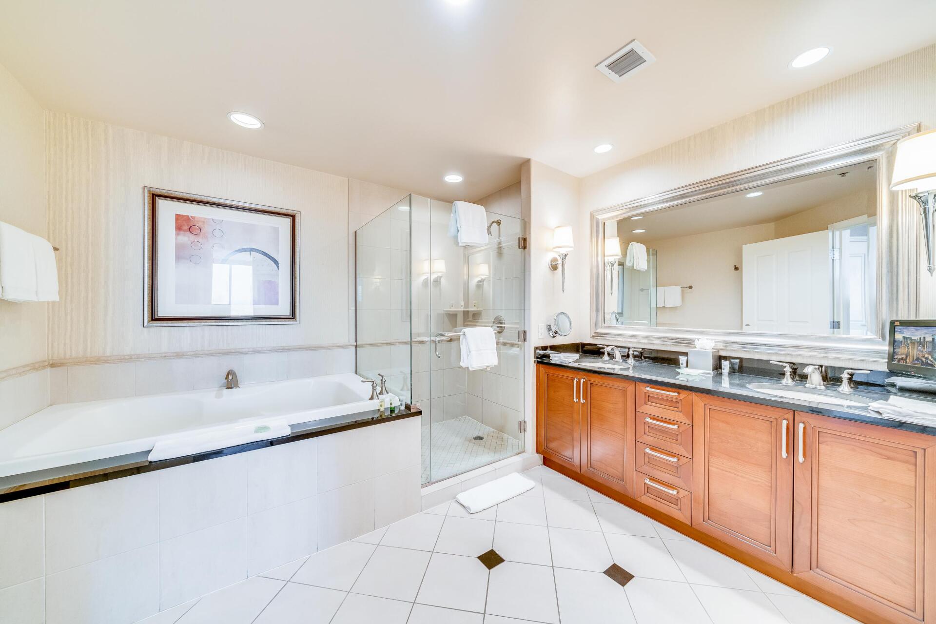 Bright bathroom with double vanity, large tub, and glass-enclosed shower in white and wood tones