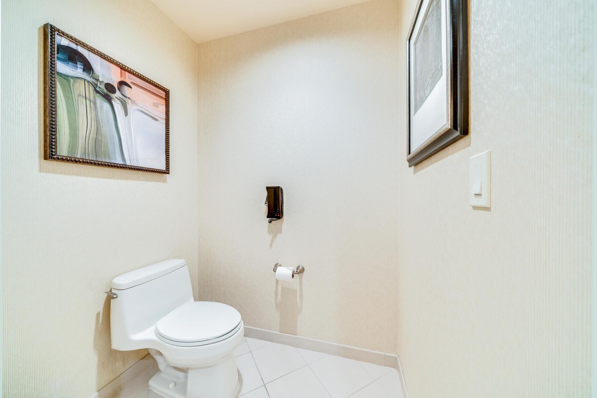 Small white bathroom with toilet, sink, towel dispenser, and framed wall art.