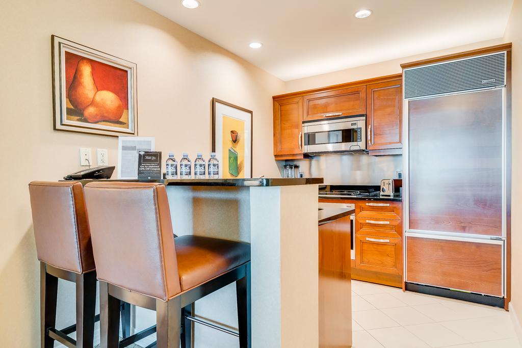 Modern kitchen with granite island, two brown bar stools, wooden cabinets, and stainless steel appliances