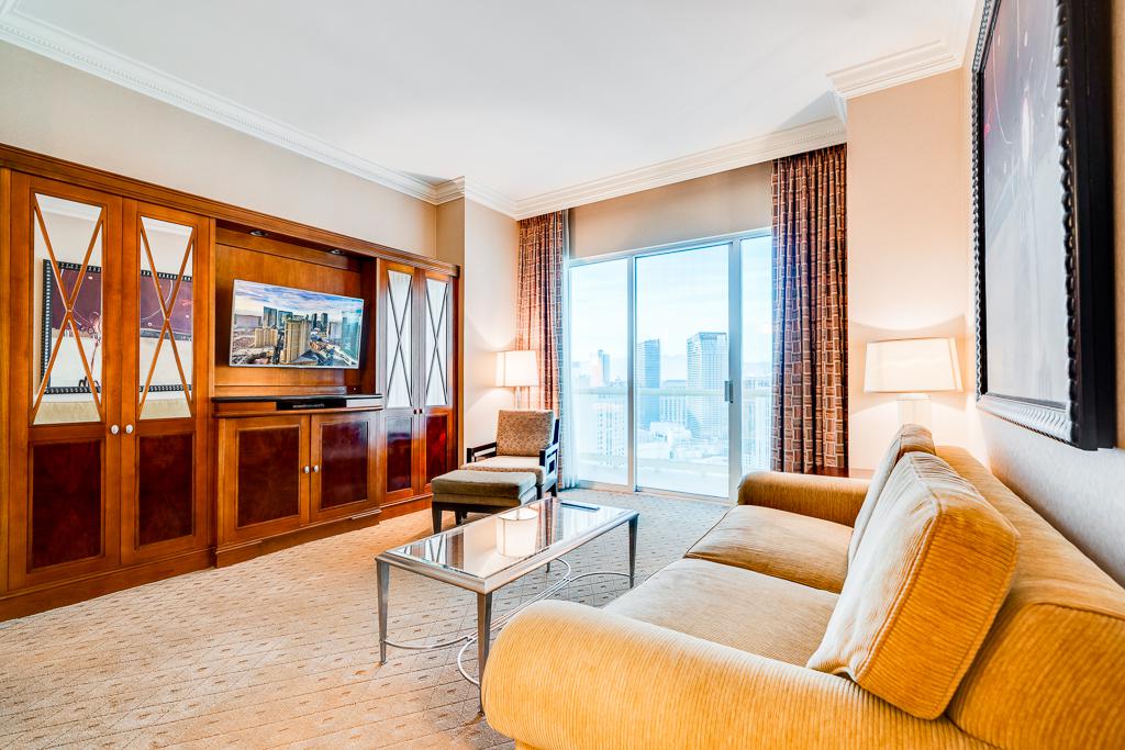 Bright living room with beige sofa, wood cabinet, coffee table, and city view through large windows