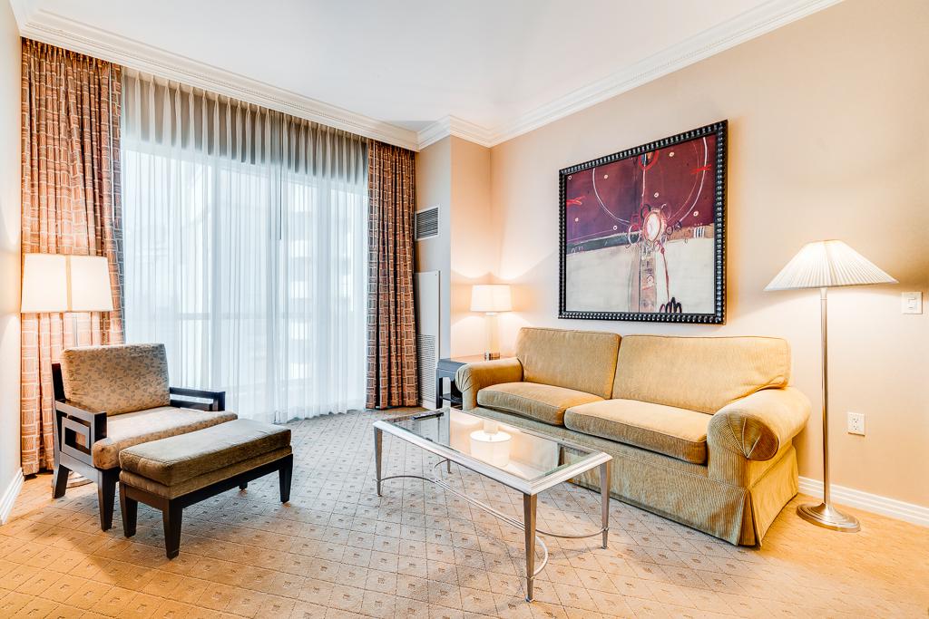 Bright hotel living room with sofa, armchair, coffee table, lamp, and large window with curtains