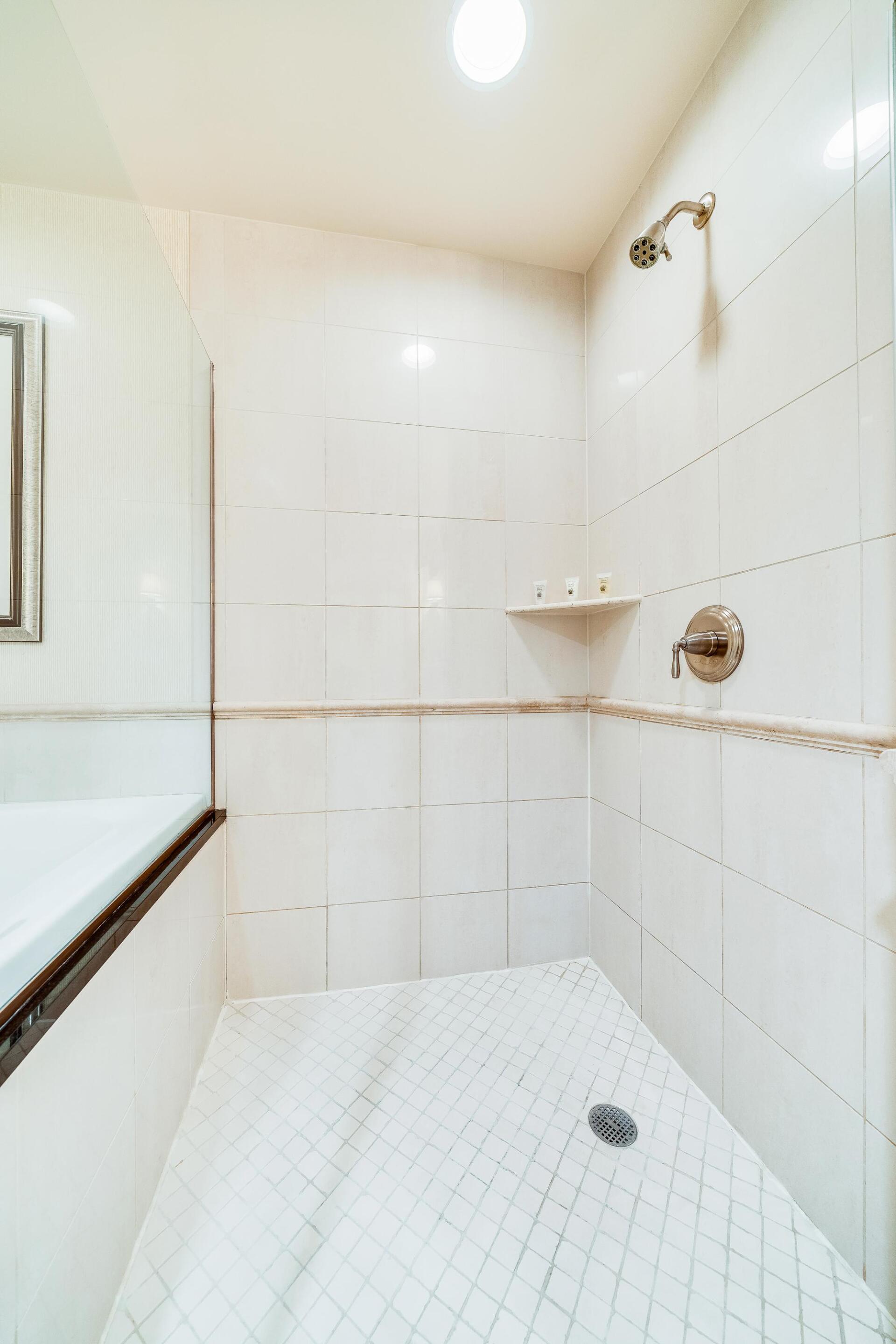 Small white tiled shower stall with a handheld showerhead and built-in corner shelf