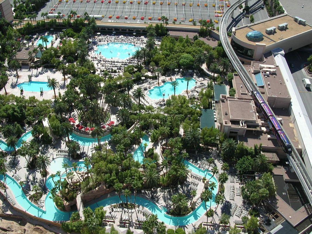 Aerial view of a resort pool area with turquoise pools, palm trees, and surrounding walkways.