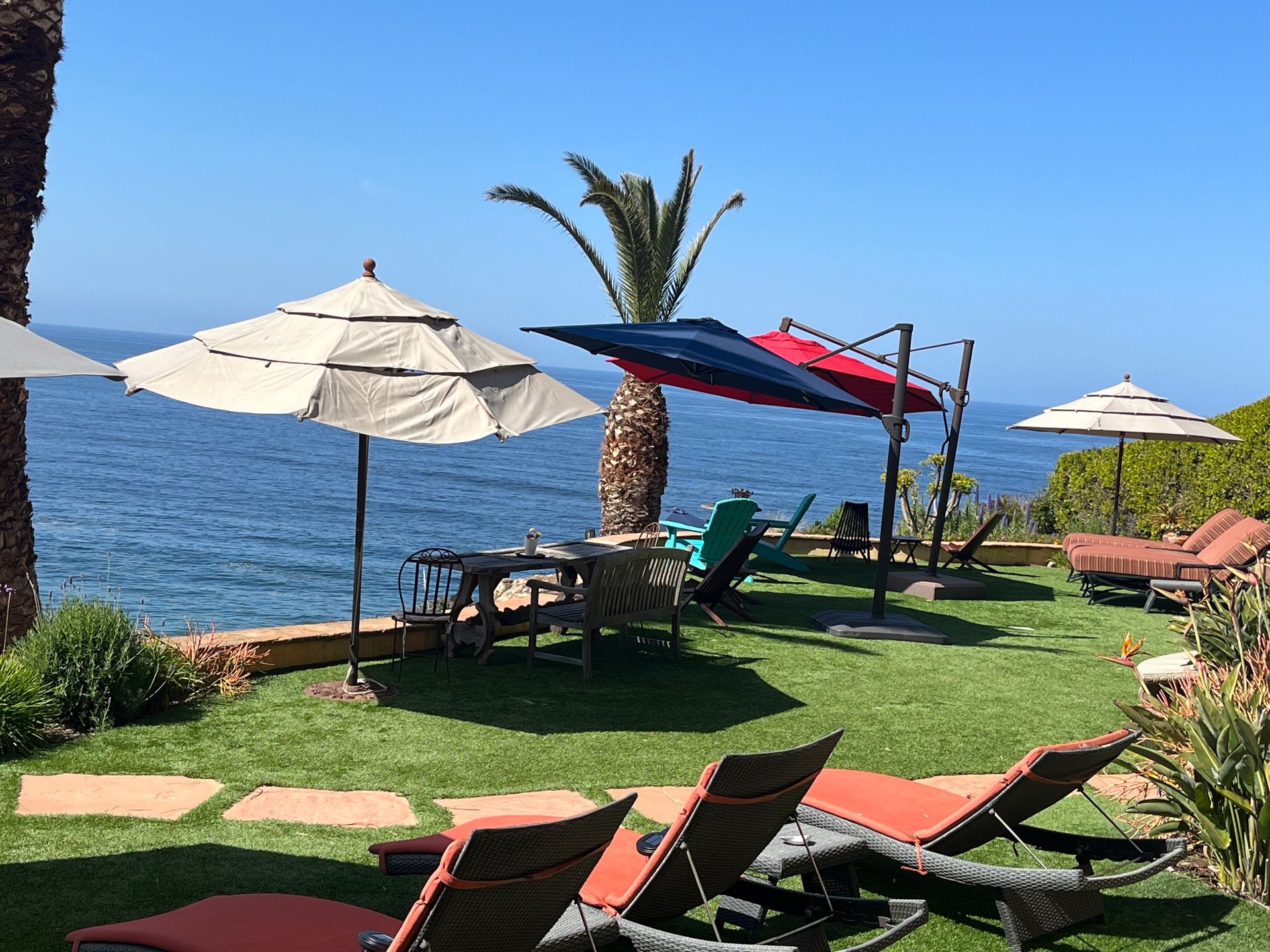 Beachside lounge chairs and umbrellas on a grassy lawn overlooking the ocean
