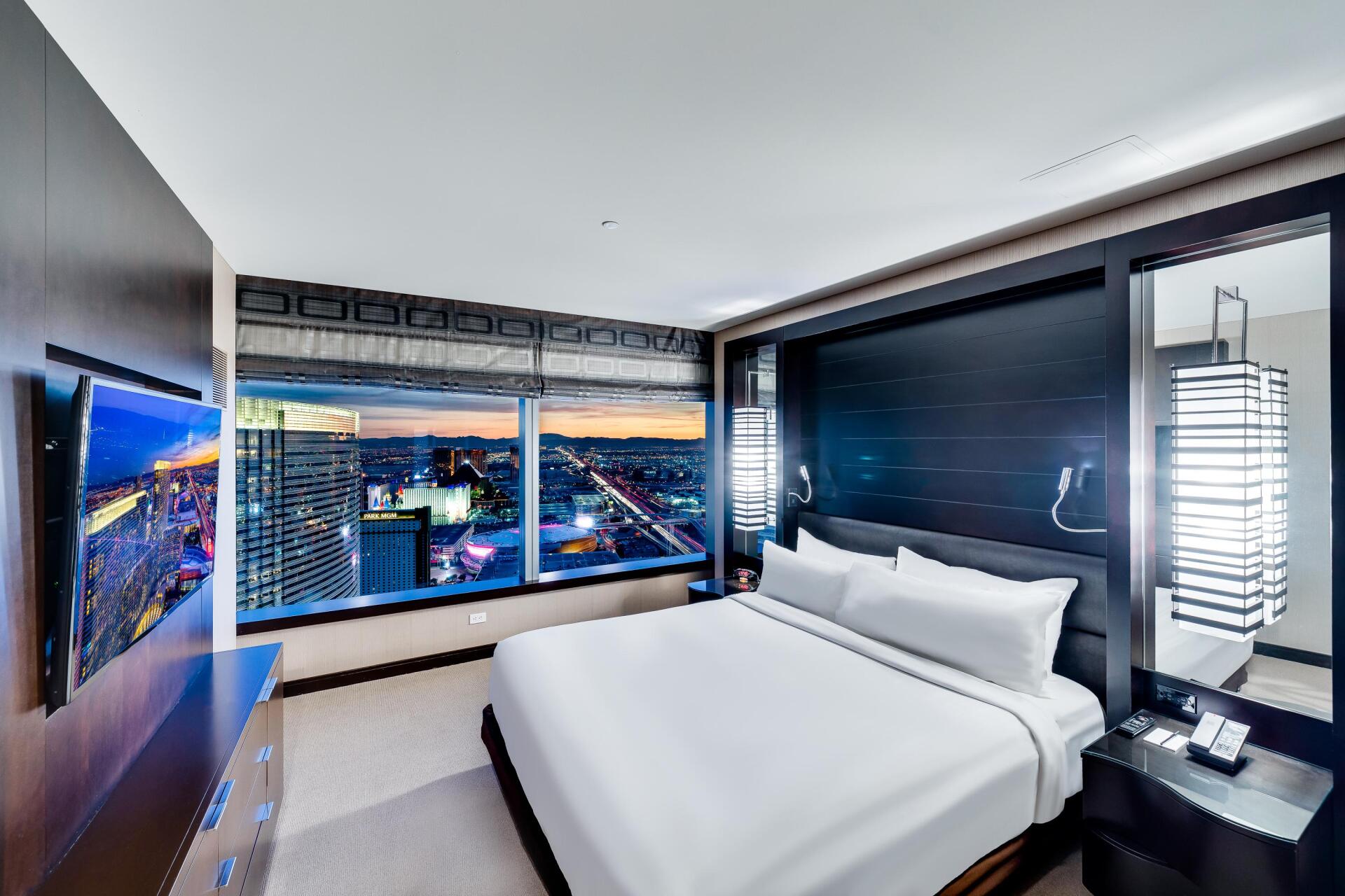 Modern hotel bedroom with large windows overlooking a city at night