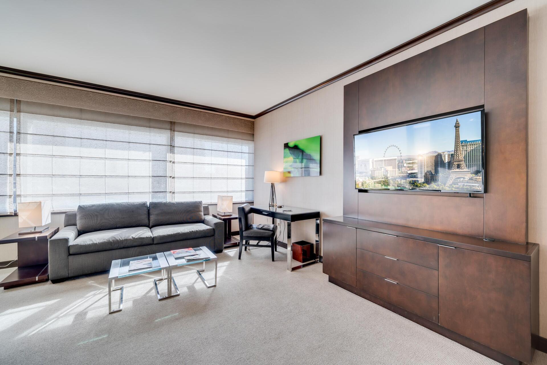 Modern living room with gray sofa, glass coffee table, wall art, and large windows