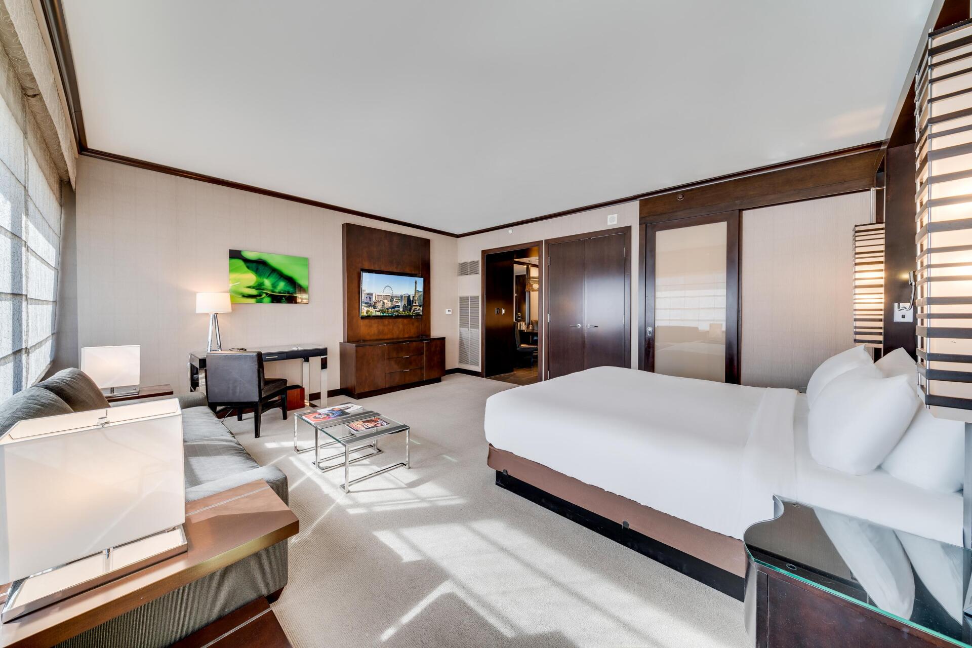Modern hotel room with two beds, desk, TV, and large window, in light neutral tones