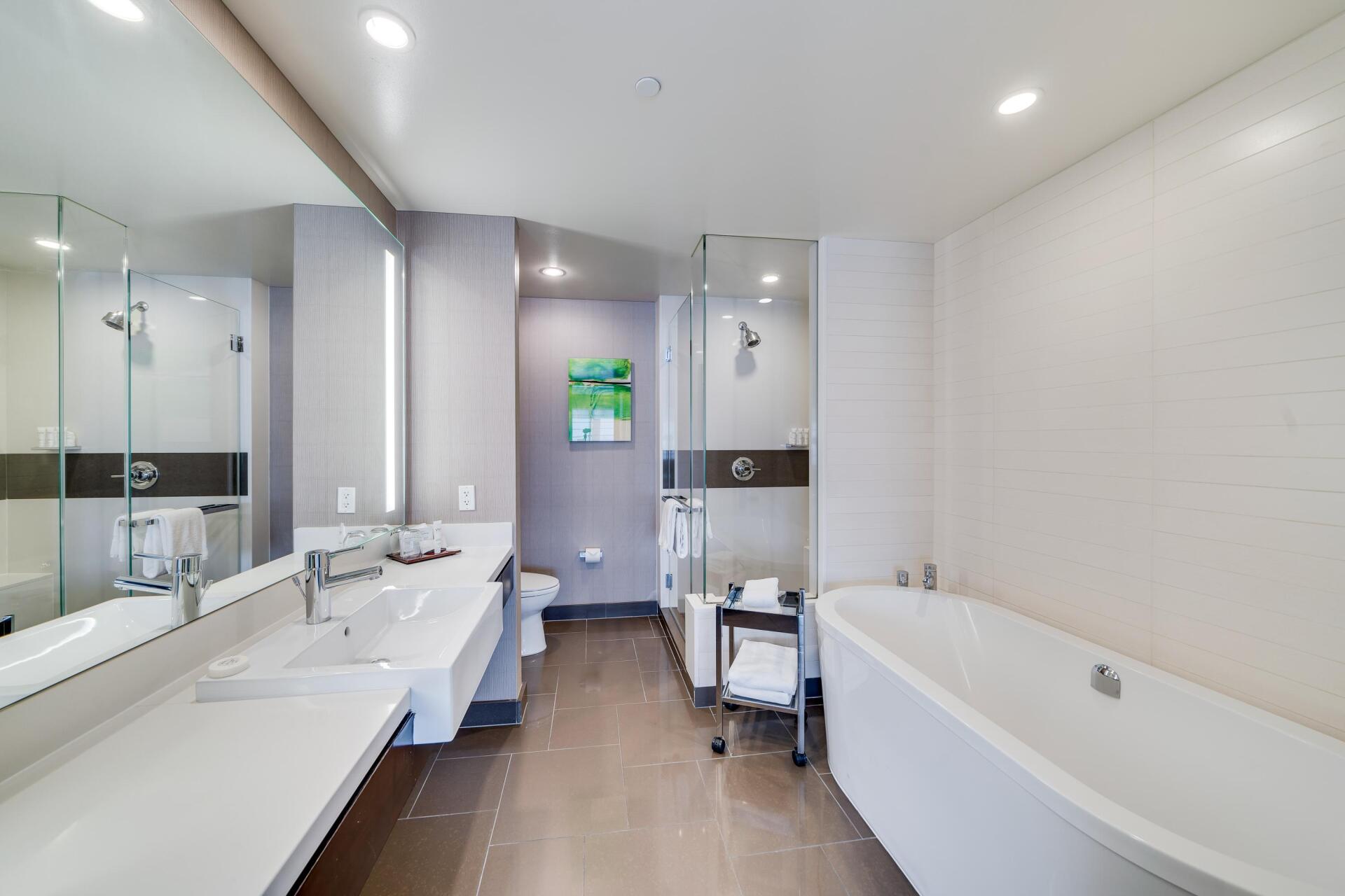 Modern bathroom with double sink vanity, large mirror, bathtub, and neutral tile walls