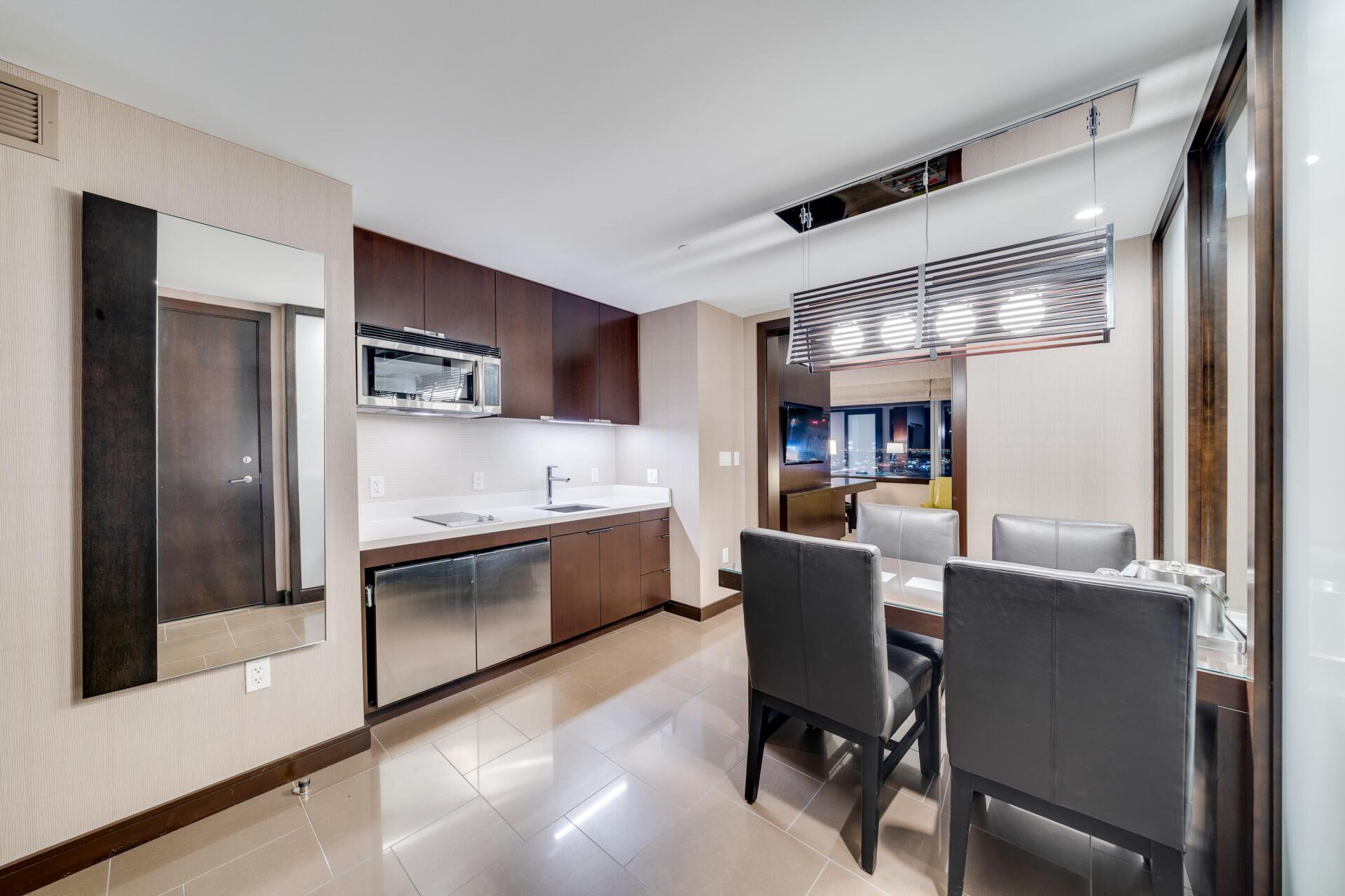 Modern dining area with glass table, dark chairs, and kitchenette in a bright apartment