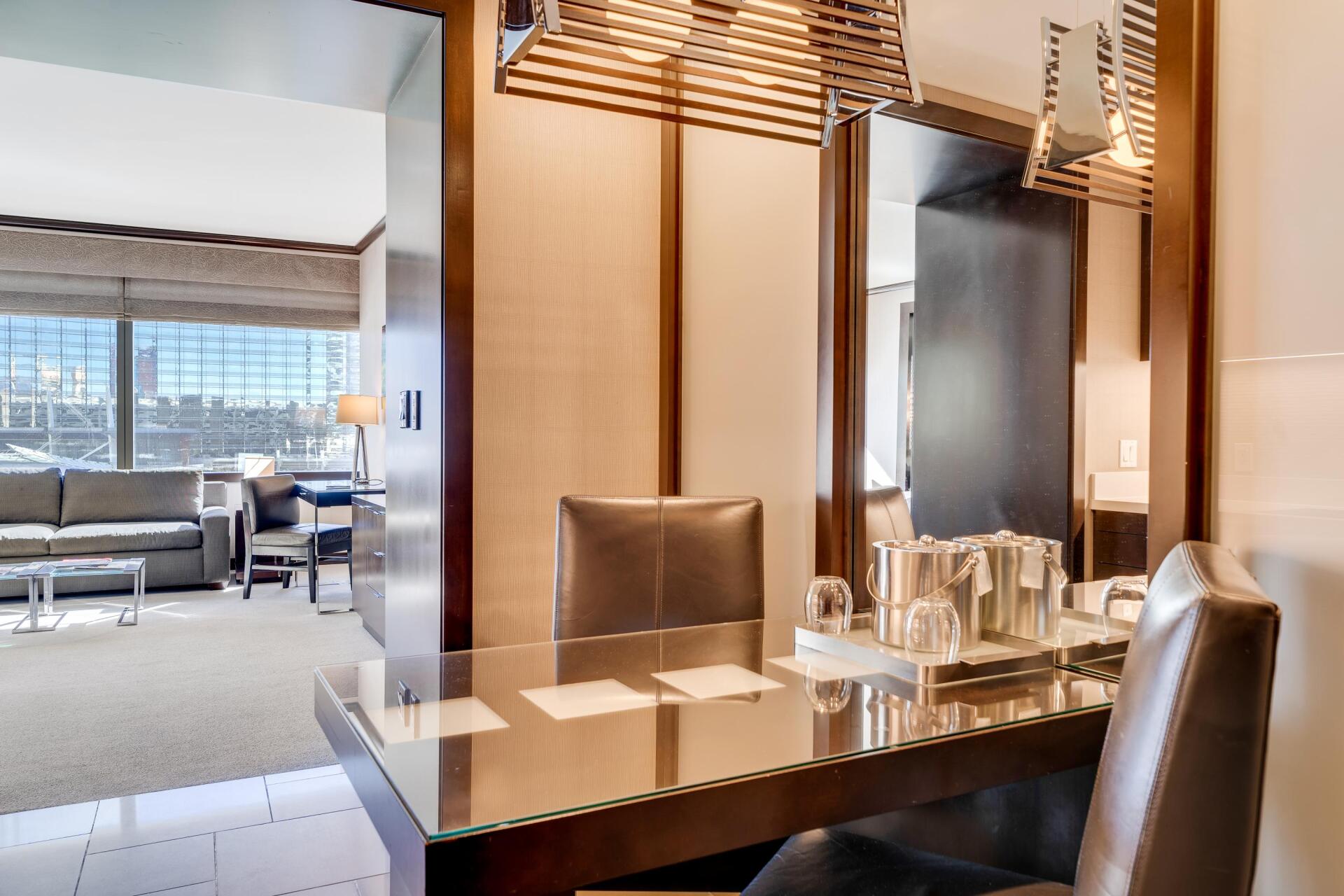 Modern hotel room with a desk, two chairs, and large windows overlooking a city.