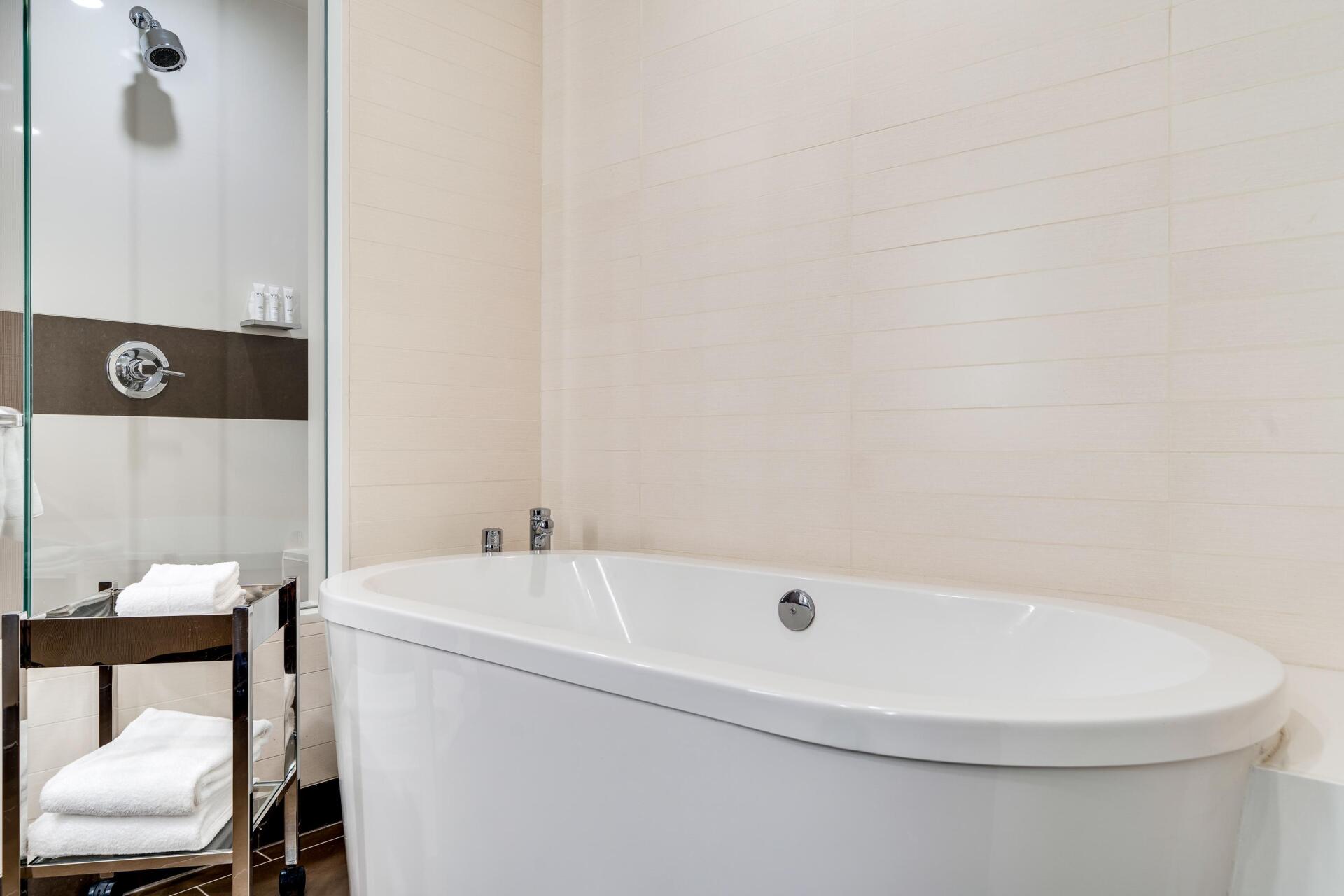 Modern bathroom with a freestanding white bathtub, glass shower, and shelving with towels