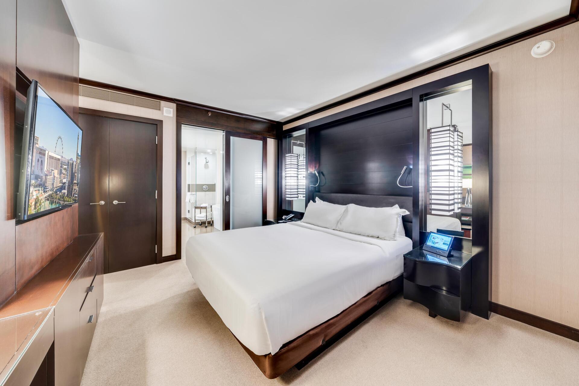 Modern hotel bedroom with a white bed, wall TV, and mirrored bathroom door
