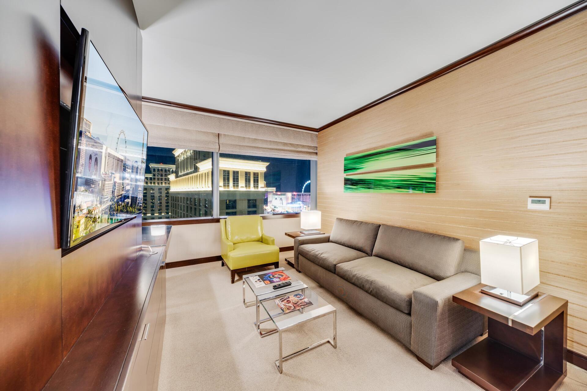 Modern living room with gray sofa, green chair, wall art, and large window view of city buildings.