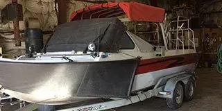 White and black speedboat on a trailer inside a garage, with a red canopy cover.