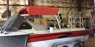 Red-and-white motorboat on a trailer inside a storage shed, with a red cover over the bow.