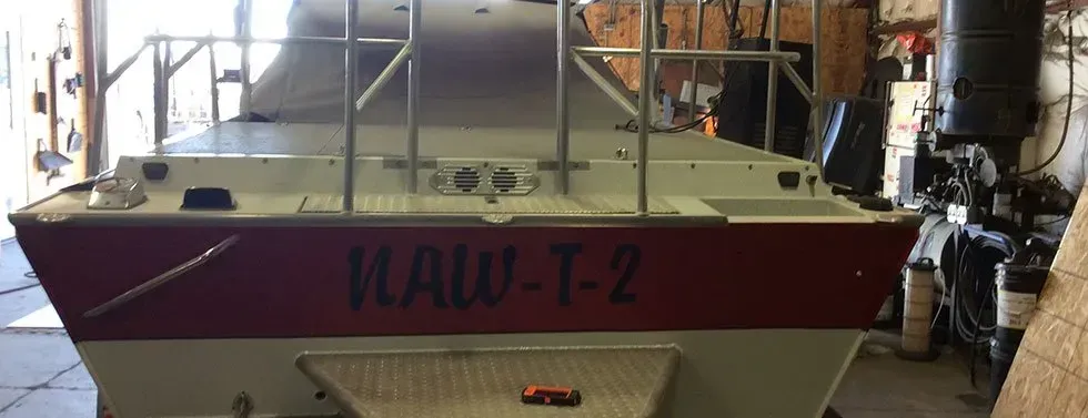 Purple-and-white boat in a workshop, front view with “WAV-T-Z” on the bow