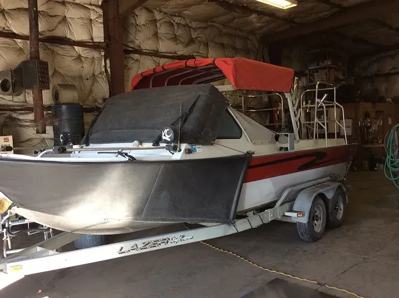 White and red speedboat on a trailer inside a storage garage, with a covered bow.