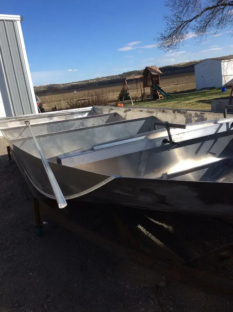 Damaged metal trailer in a driveway under a clear blue sky, with bent silver panels and a black tarp.