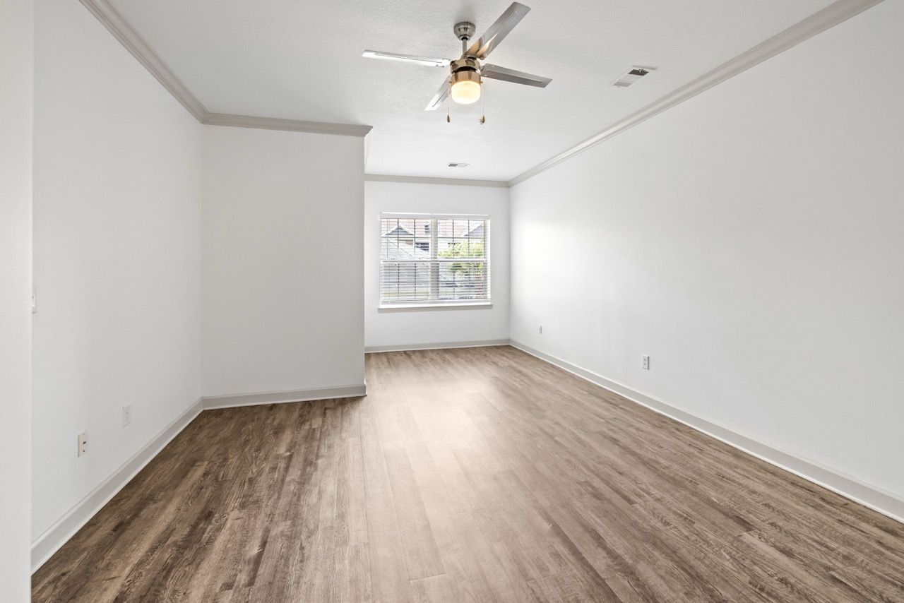 Empty living room with white walls, a window, a ceiling fan, and wood-look vinyl flooring.