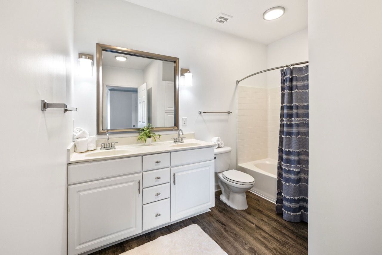 Bathroom with a double vanity, mirror, toilet, and tub/shower with blue curtain.