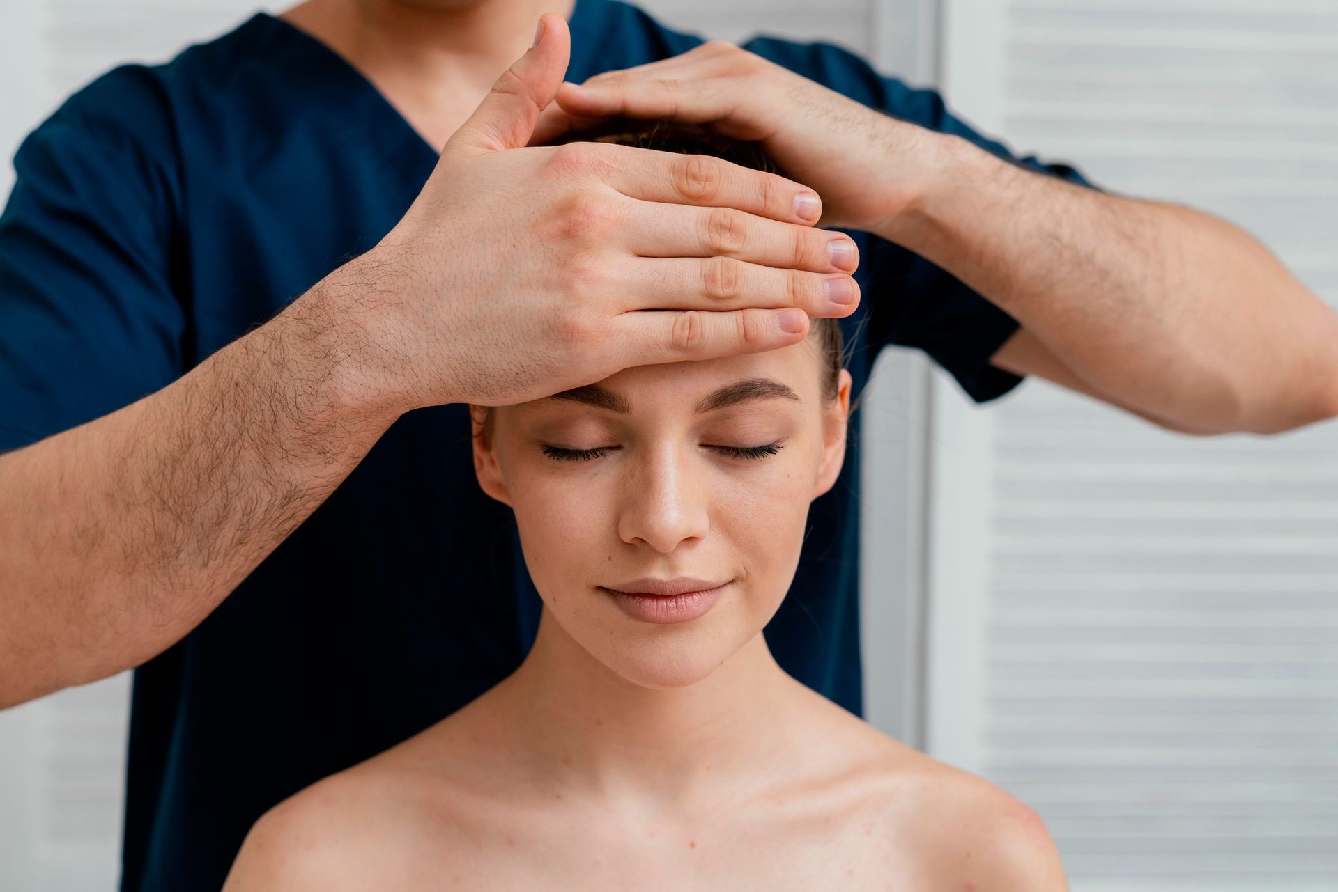 Person receiving a head massage from a therapist in a blue uniform