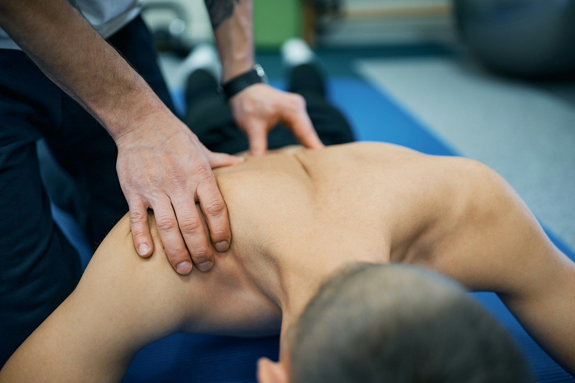 Physical therapist massaging a patient’s bare upper back on a treatment table